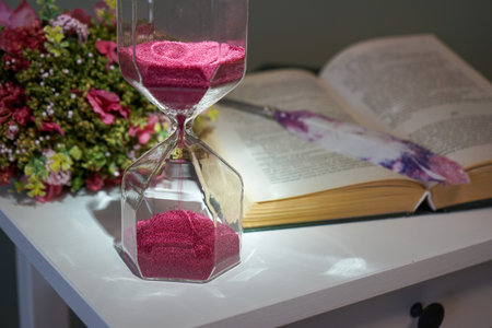 hourglass on the nightstand next to an open book, a feather and a bouquet