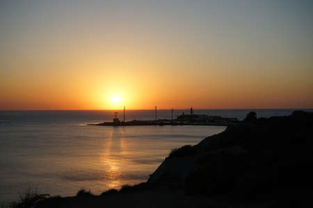 lighthouse on the island at sunset and a beautiful shadow on the sea in the light of the setting sunの写真素材