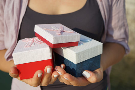 a woman holds in beautiful hands with a well-groomed manicure many multi-colored gift boxes of...