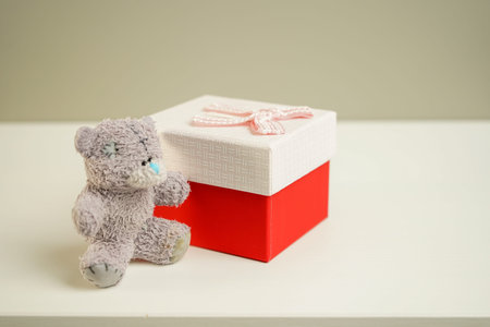 vintage teddy bear sitting next to a red gift box on a bedside table against a gray wall background