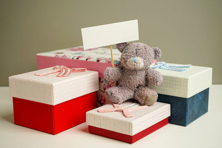 teddy bear sits on the bedside table next to colorful gift boxes of different sizes and holds a sign...