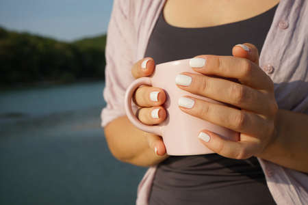 a woman drinks coffee while holding a mug in her hands in the morning at dawn outdoorの写真素材