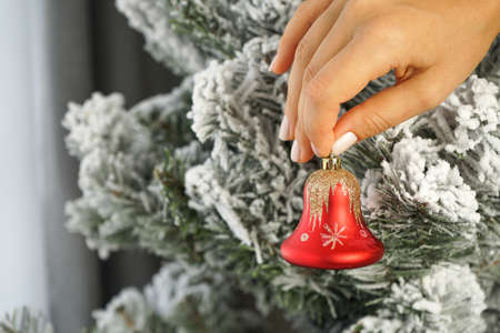 a woman's hand holds a Christmas tree toy red Christmas bell, going to decorate the Christmas tree with it from copy spaceの写真素材