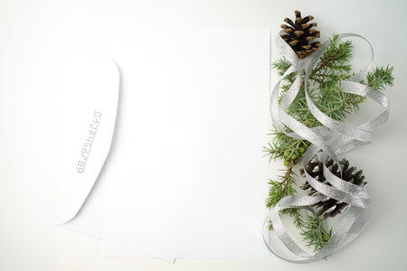 Christmas composition of coniferous tree branches, pine cones and silver ribbon next to envelope as...