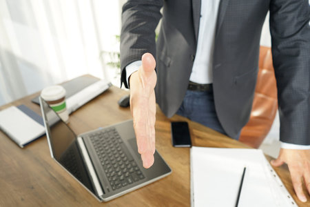 the male businessman extends his hand to the partner for a handshake as a sign of reaching an...