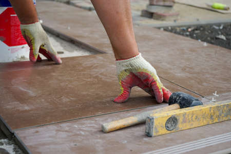 a male worker in construction gloves lays tiles on the street using a hammer and a levelの写真素材