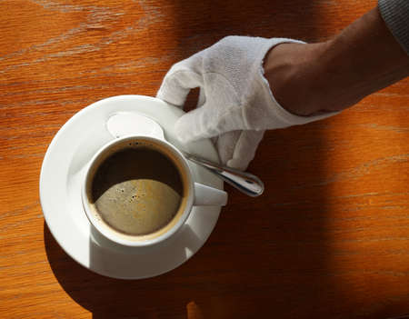 a white-gloved waiter serves coffee in a white Cupの写真素材