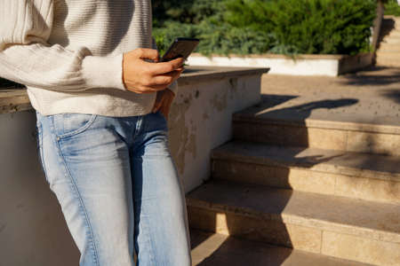 a woman in a white knitted sweater and jeans with a smartphone during a walk in the autumn Parkの写真素材