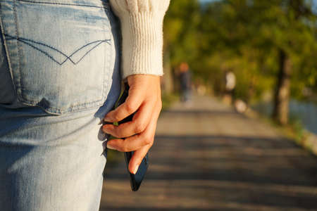 a woman in a white knitted sweater and jeans holds a smartphone in her hand while walking in an autumn Parkの写真素材