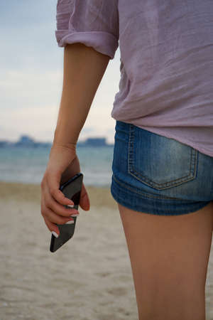 beautiful woman stands on the sea beach and holds a phoneの写真素材