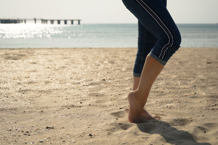 a woman stands barefoot on the sand by the sea