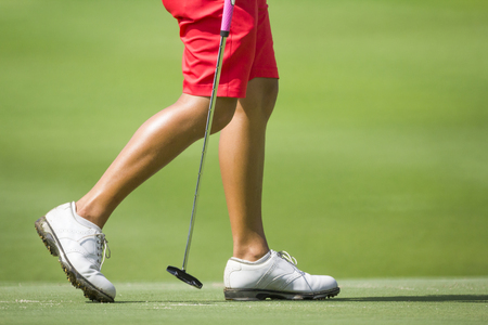 Female golfers walking on green with putter.の写真素材