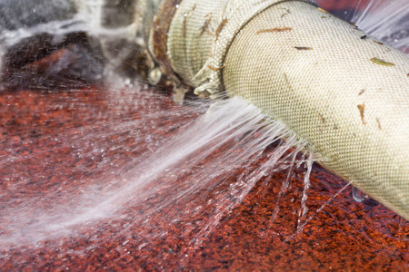 wasting water - water leaking from hole in a hoseの写真素材