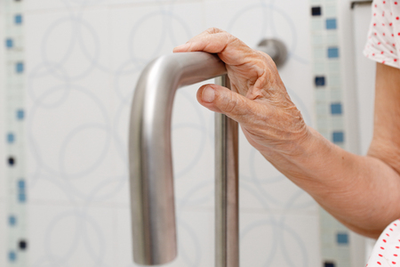 Elderly woman holding on handrail in toilet.の写真素材