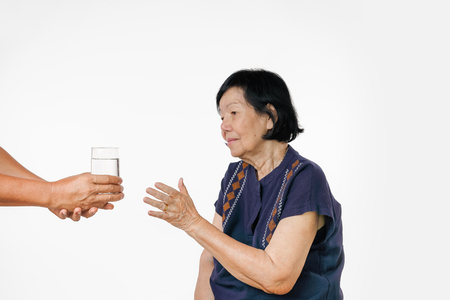 elderly woman gets a glass of water and her pills from caregiverの写真素材