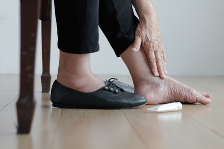 Elderly woman putting cream on swollen feet before put on shoesの写真素材