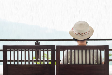 Rear view of middle aged woman on bench in rainy dayの写真素材