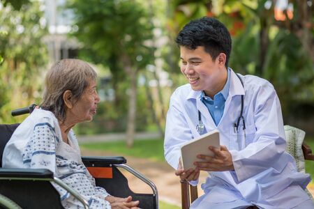 Asian doctor talking with elderly female patient on wheelchairの写真素材