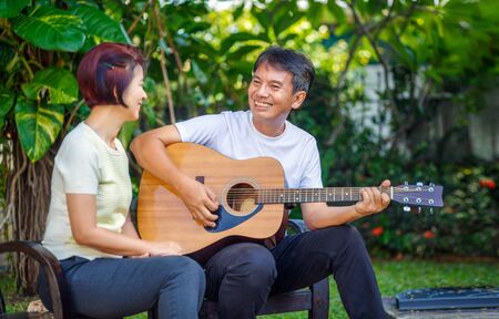 Middle aged  couple playing guitar while relax sitting on bench in backyard.の写真素材