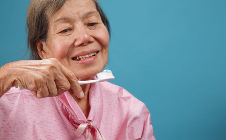 Caregiver take care asian elderly woman while using dental fross stick.