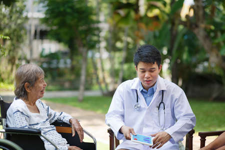 Asian doctor talking with elderly female patient on wheelchairの写真素材