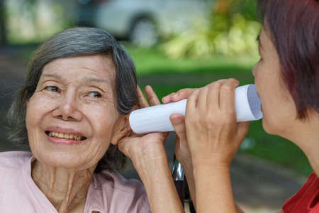 Daughter talking to hearing impaired elderly woman , using paper tubeの写真素材