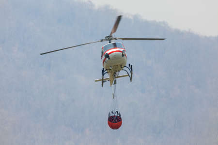 Firefighting  helicopter carrying  water bucket for extinguish forest fire,   comeback at lake to filling waterの写真素材