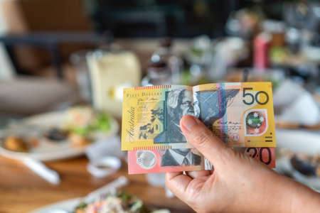 Woman's hand holding Australian notes to make a payment in restaurant.の写真素材