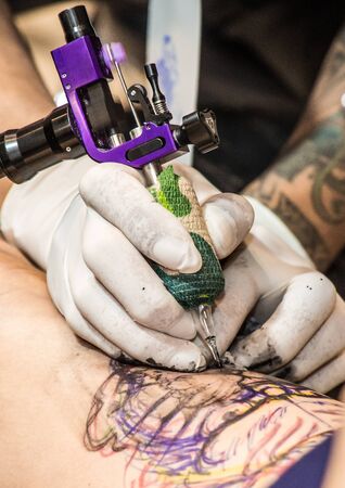 Professional tattoo artist makes a tattoo on a man's back with a purple electronic tattoo machine.の写真素材
