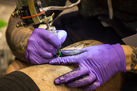 Professional tattoo artist makes a tattoo on a man's leg with an electronic tattoo machine.の写真素材