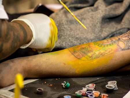 Professional tattoo artist makes a tattoo on a man's arm.Master tattoo draws the yellow paint on the clients tattoo.の写真素材