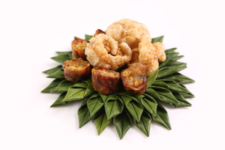Northern Thai Food on white background; pork rind and Thai spicy sausage on green banana leaf basket.の写真素材