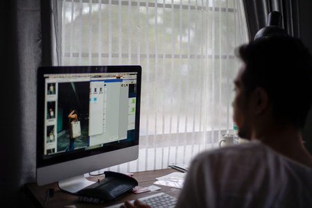 Silhouette unkown man using a desktop computer in front of white translucent curtain