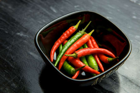 Red and green chilli peppers in black bowl on black backgroundの写真素材