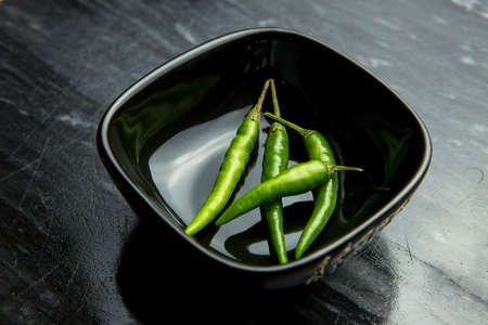 Green chilli peppers in black bowl on black backgroundの写真素材