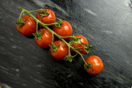 Lot of whole fresh red coctail tomato flatlay on an black stone plateの写真素材