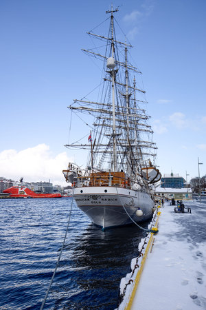 Bergen, Norway - April 05, 2021: Big white sailing ship in dock on water seen from rear with snow in...