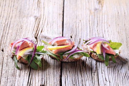 Salmon open faced sandwiches garnished with red onion and lemonの写真素材