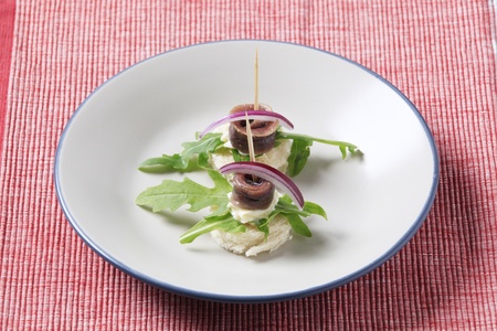 Anchovy canapes garnished with arugula and onionの写真素材