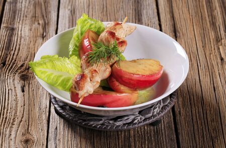 Grilled chicken skewer and slices of baked apple の写真素材
