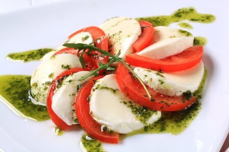 Slices of mozzarella cheese and tomato seasoned with pesto sauceの写真素材