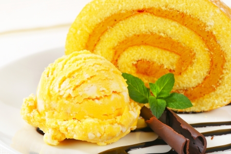 Slice of Swiss roll with yellow ice cream and chocolate sauceの写真素材