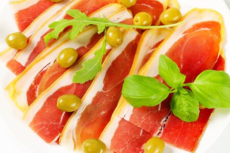 Thin slices of prosciutto crudo and marinated green olivesの写真素材