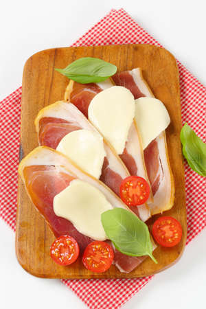Sliced prosciutto crudo and mozzarella with fresh basil and tomatoesの写真素材