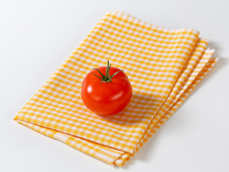Fresh red tomato on checked yellow tea towelの写真素材