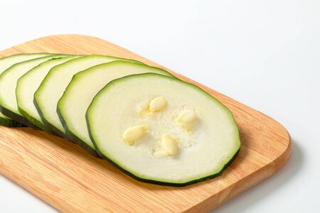 six thin slices of fresh zucchini on a wooden cutting boardの写真素材
