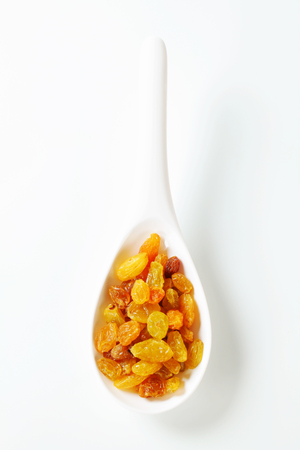 Golden-coloured raisins on a white spoonの写真素材