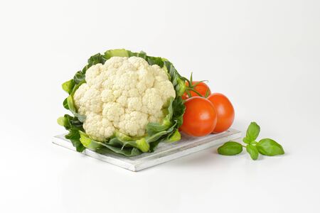 head of fresh cauliflower and tomatoes on wooden cutting boardの写真素材