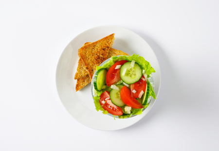 bowl of mixed vegetable salad and slices of toasted bread on white plateの写真素材