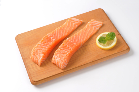 two raw salmon fillets on wooden cutting board